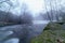 Foggy winter landscape, river with water falling down a waterfall, rocks and bare trees. Long exposure photo