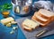 Foil wrapped processed cream cheese, table knife and slice of bread on a cutting board over blue wooden table. Small