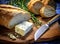 Foil wrapped processed cream cheese, table knife and slice of bread on a cutting board over blue wooden table. Small