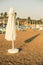 Folded beige beach umbrella on the beach and its shadow