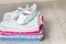 Folded pink and white bodysuit with shoes on it grey wooden background. diaper for newborn girl. Stack of infant clothing. Child