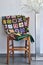 Folded quilt on a chair and floor lamp against a neutral wall