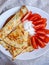 Folded and rolled thin golden pancakes with dilles, sour cream and tomatoes