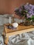 Folding table on the bed with candle in shell form, candels in vintage brass candlesticks and bunch of lilac flowers.