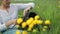 Folk crafts. Handmade. Young woman weaves rattar baskets sitting in the grass. Yellow flowers in the foreground