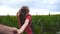 Follow me shot of young woman in red dress pull her boyfriend on corn field. Happy girl holding male hand and running