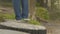 Follow shot from rear back of woman legs wearing jeans walking leisurely on concrete stump in natural park during summer.