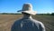 Follow to unrecognizable young male farmer in hat and shirt walking on his field at sunny summer day. Blue sky at