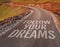 Follow your dreams motivational message on asphalt road through countryside landscape