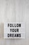 `Follow your dreams` words on a lightbox on a white wooden background, top view. Overhead, from above, flat lay. Copy space