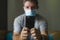 Following online news on covid-19 virus pandemic - man with face mask in home quarantine lockdown checking internet information on