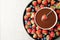 Fondue fork with strawberry in bowl of melted chocolate surrounded by different berries on light table, top view