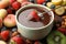 Fondue fork with strawberry in bowl of melted chocolate surrounded by other fruits on wooden table