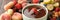 Fondue fork with strawberry in bowl of melted chocolate surrounded by other fruits on wooden table