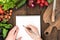 Food composition of raw vegetables, chopping board and human hand able to write something in notepad