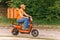 A food delivery man in orange with a protective medical mask on his face rides a moped with a food delivery bag