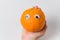 Food with Funny Faces. Orange with sad eyes. Female hand holding tangerine with eyes white background