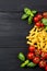 Food ingredients for Italian tortiglioni pasta with cherry tomatoes and basil leaves, black wooden background, top view with copy