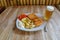 Food on white porcelain plate. Breaded fried cheese, boiled potatoes, tartar sauce, sliced tomato. Beer in glass on teak table.