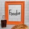 Foodie handwritten on white subway tile in orange wood frame with sweet syrup stack of homemade waffles