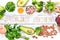 Foods that contain natural vitamin B9: Liver, avocado, broccoli, spinach, parsley, beans, nuts, on a white wooden background.