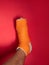 Foot with broken toe bone in orange fiberglass cast pink background. Injured fractured swollen male leg. Patient body