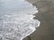 Foot prints on a black sand beach with tilt-shift blur. Surf in background. Concept for loneliness, solitude, depression