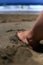 foot submerged in the sand on the beach against the waves of the ocean