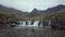 Footage of a morning view of a river with a waterfall and a mountain range covered in clouds