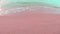 Footage of pink fine sand and ocean water wave blow on shore. smoothie white sea foam forming the cure pattern.