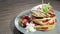 Footage of a portion of pancakes decorated with strawberries on a plate lying on a table, the shot is rotating on a table