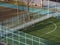 The football field in the park is fenced with a metal barrier. The park and the playing field are lit by the sun. View from above