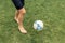 Footballer barefoot stuffs the ball on the green grass.