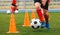 Footballer dribbling ball on training between orange cones