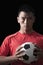 Footballer holding ball to chest, black background