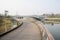 Footbridge along riverside to arch of highway bridge in sunny wi