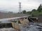 Footbridge crossing the flood alleviation weir on the river aire at knostrop leeds with electricity pylons in a rural industrial