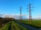 Footpath on creek dike along asphalt road, with view of masts, field and meadow