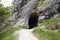Footpath leading to entrance to the cave in Jura mountains. Black hollow in rock. Mountain tunnel hiking trail, cave enter of dark