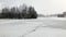 Footpath through snow-covered frozen lake in snowfall. Bare trees on shore.