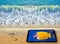 Footprint in front on blue sea coastline and cell phone with screen displaying nice yellow fish