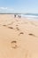 Footprints along the sand coast, a group of four people are hanging out in the beach, the ocean has just a single wave