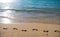 Footprints at golden sand, footsteps. Beach background. Calm beautiful ocean wave on sandy beach. Sea view from tropical