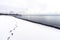 Footprints leading down a snoy beach, restful scene with cloudscape, rustic pier and blue waters