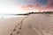 Footprints in the sand on a beautiful Australian beach lead to a colourful pink sunrise