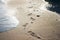 Footprints in the sand by the sea. Sea wave on the sandy shore next to the tracks. Beautiful Sunny bokeh.