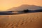 Footprints of three travelers are swept away by the wind in the desert. Mountains and blue sea in the distance