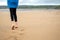 Footprints on a yellow sand in focus.Teenager girl walking on a sandy beach. The model dressed in blue jacket and black leggins.