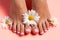 Foots of a girl in the flower buds of daisies, pink pedicure on a pink background. Top view with place for text