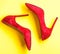 Footwear with thin high heels, stiletto shoes, top view. Shoes made out of red suede on yellow background. Pair of